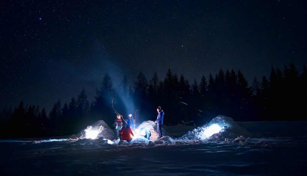 Magical night scene with adventurers gathered around a fire near their igloos under a starry sky, the ultimate winter adventure when deciding what to do in Slovakia.
