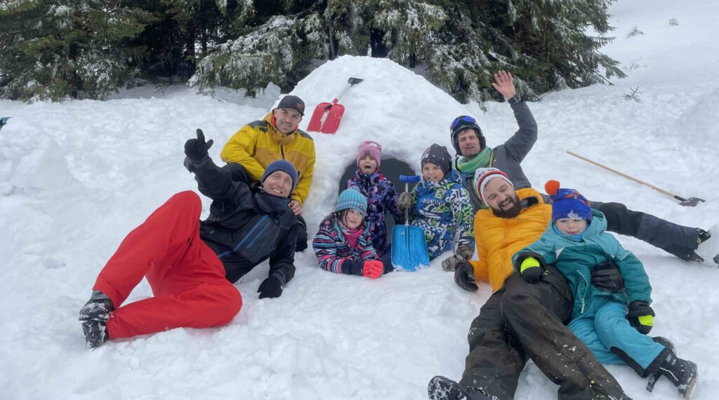 Smiling families and friends posing next to a handmade igloo in the High Tatras, a highlight of active holidays for those seeking a unique winter adventure and what to do in Slovakia.